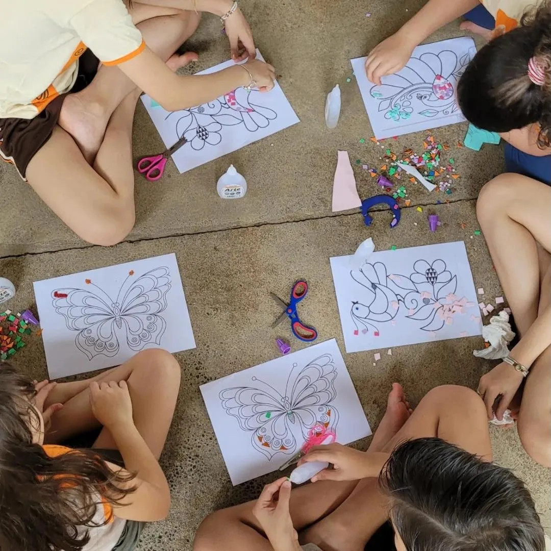 Crianças sentadas no chão fazendo mosaico de papel sobre desenhos de borboletas