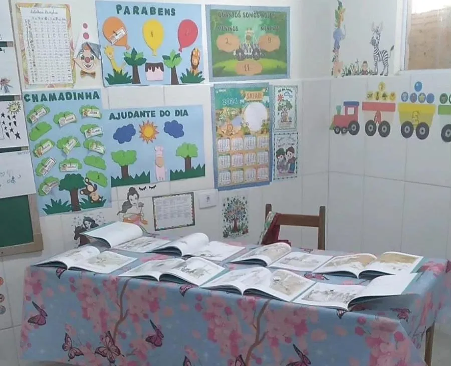 Mesa com livros abertos numa sala decorada com trabalhos das crianças